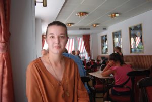 Nina Walloschke, musiker, kan uppleva hur ljudmiljön påverkar smaken av mat och dryck. På bilden sitter hon på en restaurang där andra gäster syns i bakgrunden.